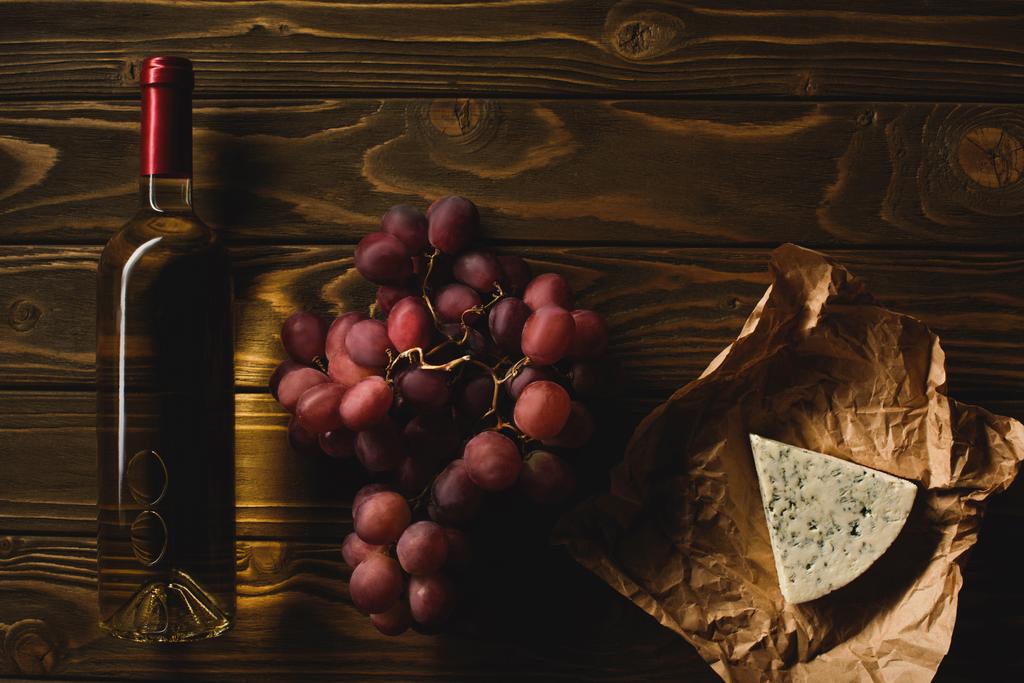 bovenaanzicht van fles witte wijn met hapjes op houten tafel - Foto, afbeelding