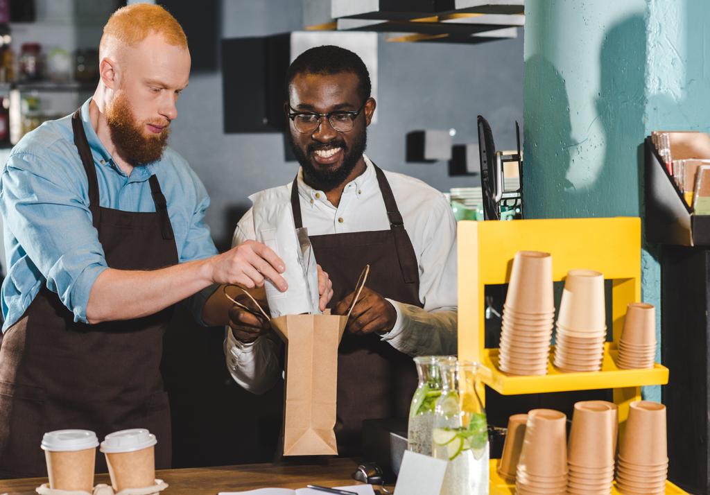 усміхнені молоді багатоетнічні власники кав'ярні роблять замовлення на паперовий мішок
 - Фото, зображення