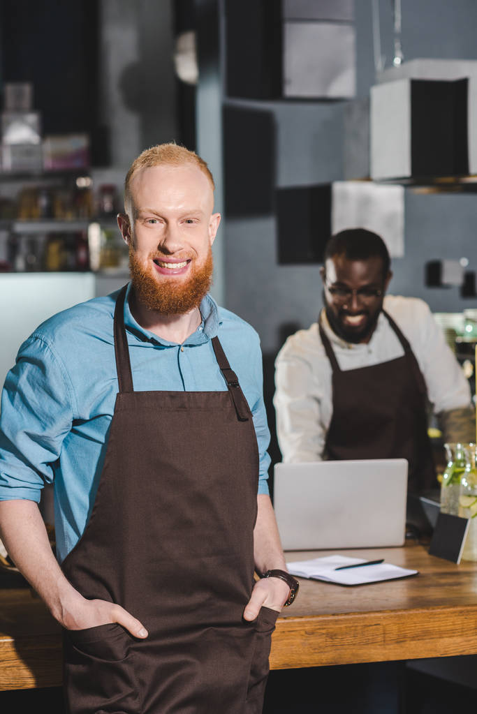 souriant jeune homme barista dans tablier avec collègue dans un café
  - Photo, image