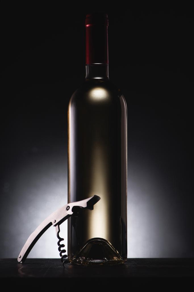 Nahaufnahme einer Flasche köstlichen Weißweins auf Schwarz mit Korkenzieher - Foto, Bild