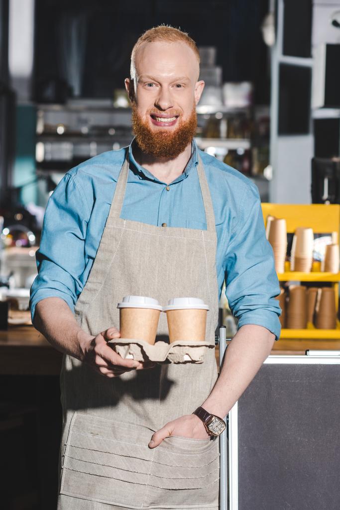 uśmiechnięty mężczyzna barista posiadania dwóch jednorazowych kubków kawy  - Zdjęcie, obraz