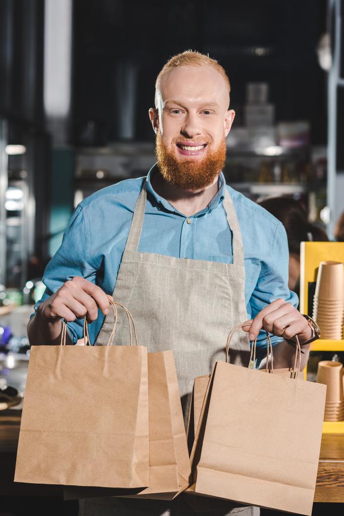 fiatal férfi barista kötényt tartja a papír táskák kávézóban  - Fotó, kép