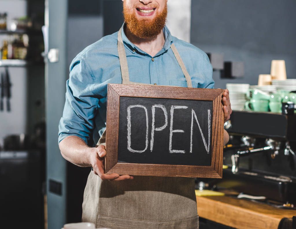 cropped image of young male barista holding chalkboard with lettering open in coffee shop - Photo, Image