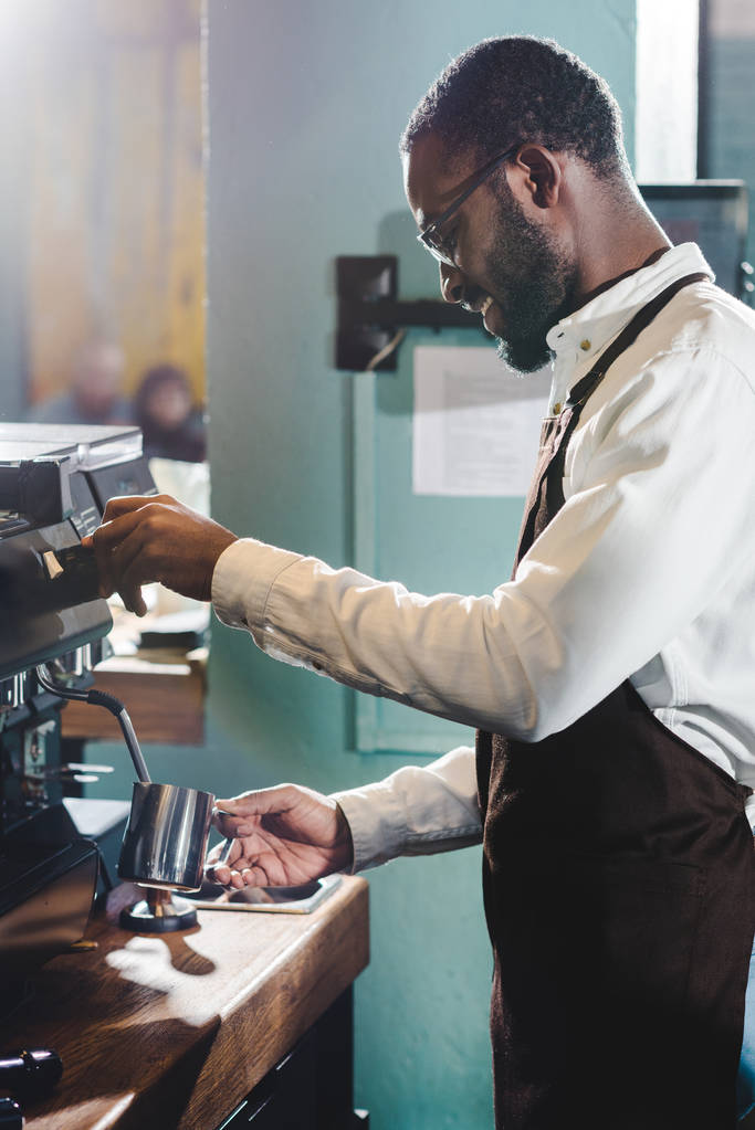 side view of happy young african american barista in eyeglasses making coffee at coffee machine  - Photo, Image