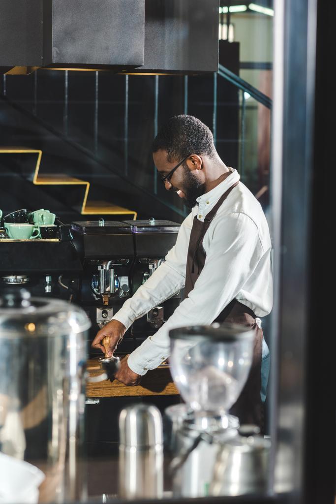 boční pohled na usmívající se mladé afroamerické barista v brýlích vaření kávy v kávovaru  - Fotografie, Obrázek