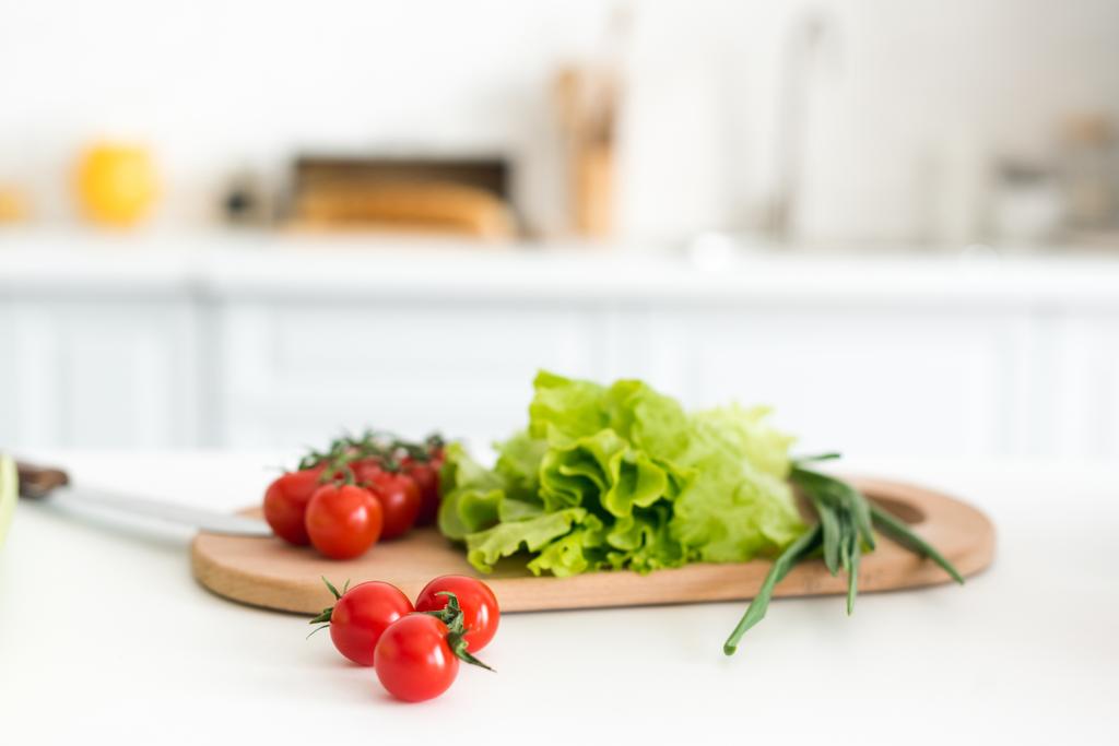 Kirschtomaten und Salatblätter auf Schneidebrett in der Küche - Foto, Bild