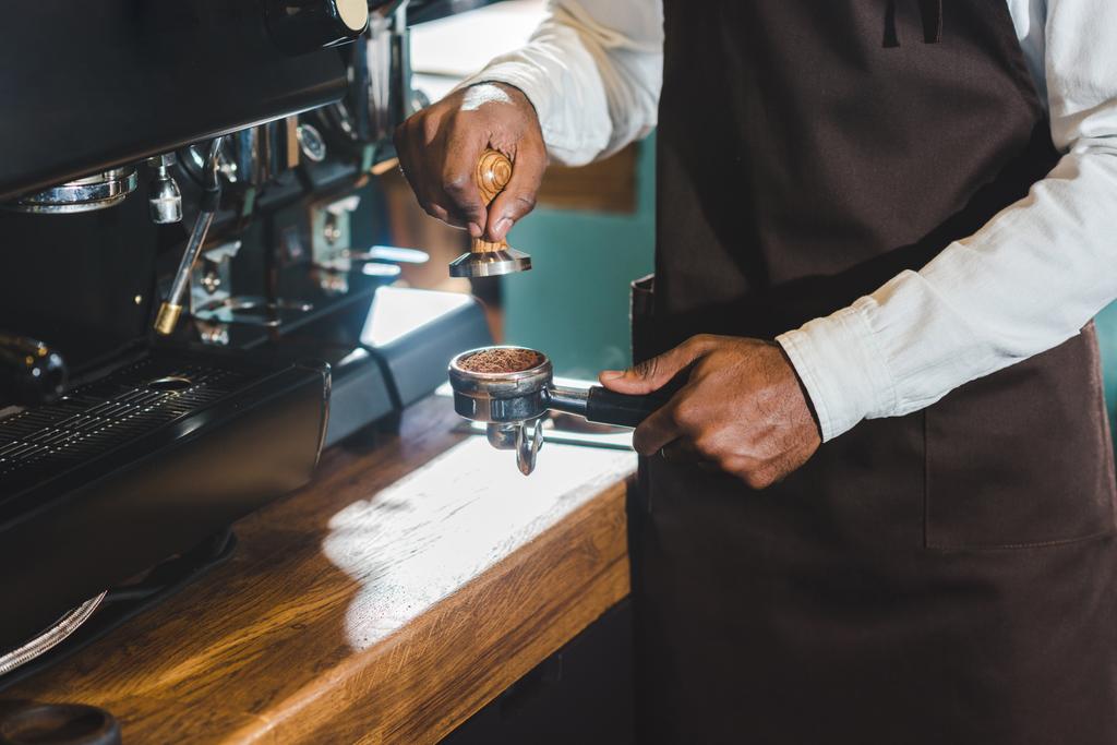 アフリカ系アメリカ人のバリスタ コーヒー マシンでコーヒーを作るエプロンのショットをトリミング  - 写真・画像