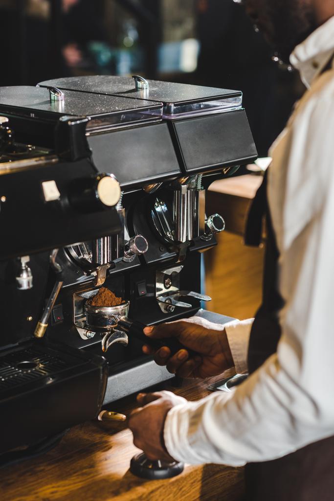 コーヒー マシンでコーヒーを準備するエプロンでアフリカ系アメリカ人のバリスタのショットをトリミング - 写真・画像