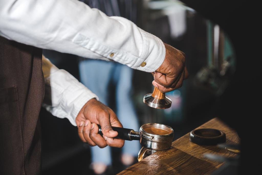 foto recortada de barista afroamericano en delantal haciendo café en la cafetería
 - Foto, imagen