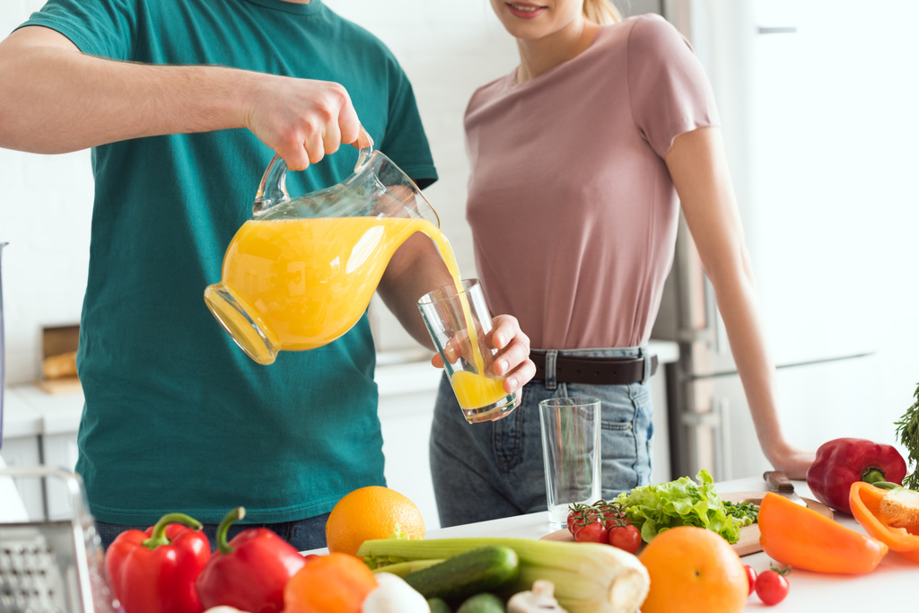 περικομμένη εικόνα vegan φίλο έκχυση φρέσκο χυμό σε ένα ποτήρι στην κουζίνα - Φωτογραφία, εικόνα