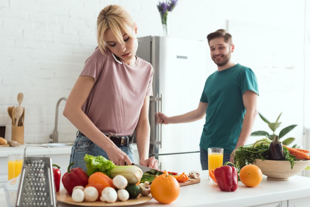 vegan girlfriend talking by smartphone while cooking salad at kitchen - Photo, Image