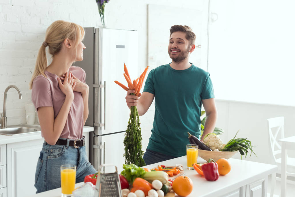 vegan φίλο παρουσιάζοντας μπουκέτο με καρότα στη φίλη στην κουζίνα - Φωτογραφία, εικόνα