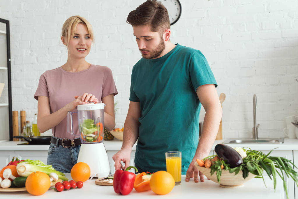 キッチンにジューサーで野菜ジュースを準備するビーガンのカップル - 写真・画像