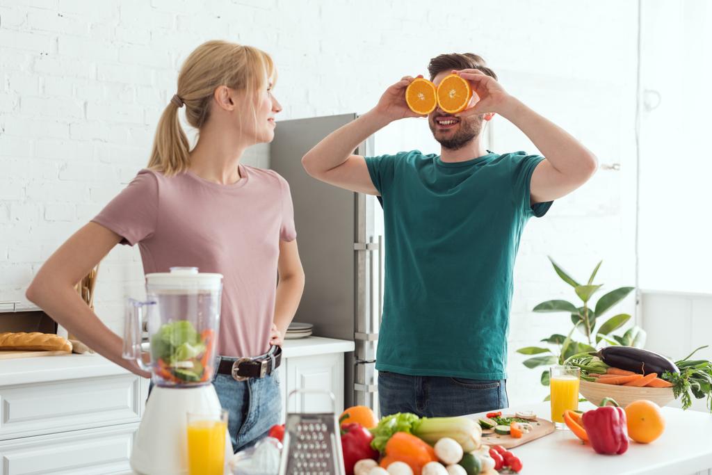 namorado se divertindo e cobrindo os olhos com peças de laranja na cozinha, conceito vegan
 - Foto, Imagem