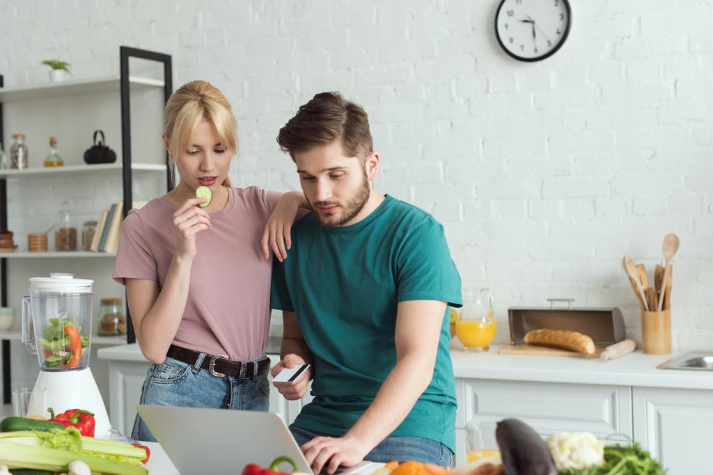 Porträt eines veganen Paares, das zu Hause in der Küche gemeinsam Laptop benutzt - Foto, Bild