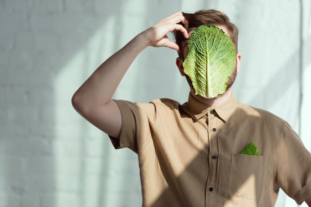 затьмарений вид на стомленого чоловіка з солоним капустяним листом на обличчі, концепція веганського способу життя
 - Фото, зображення