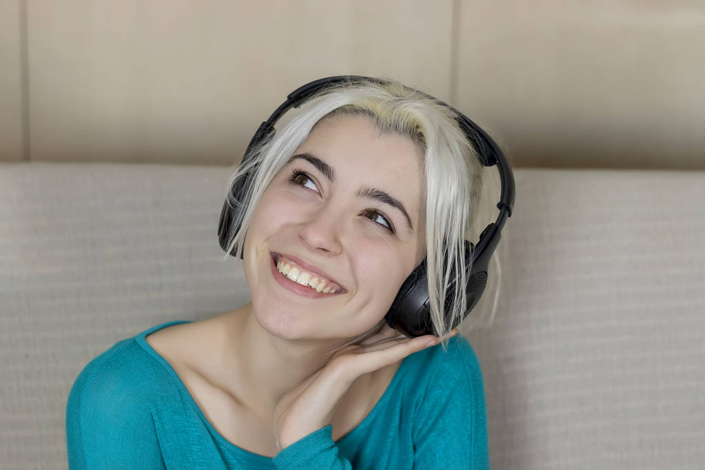 Szczęśliwy blondynka młoda kobieta siedzi na kanapie z słuchawki listeni - Zdjęcie, obraz
