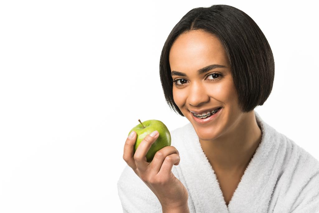 Afro-Amerikaanse meisje met tandheelkundige accolades houden van groene appel, geïsoleerd op wit - Foto, afbeelding