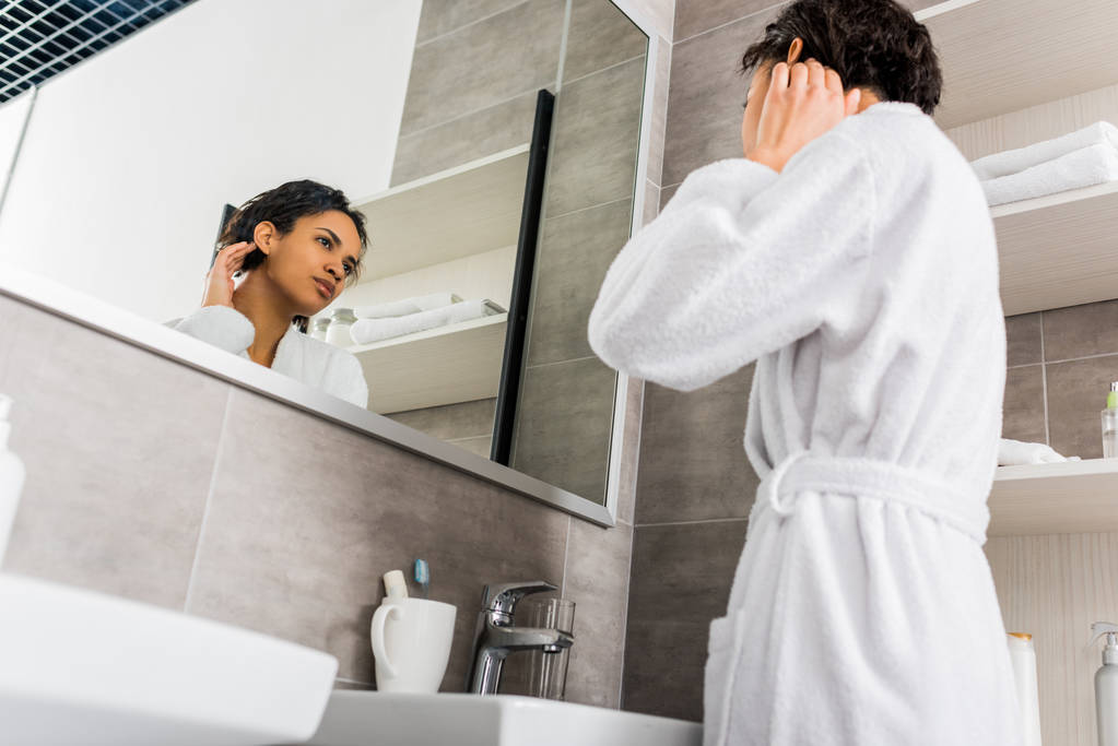 belle afro-américaine fille regardant sa peau propre dans le miroir dans la salle de bain
  - Photo, image
