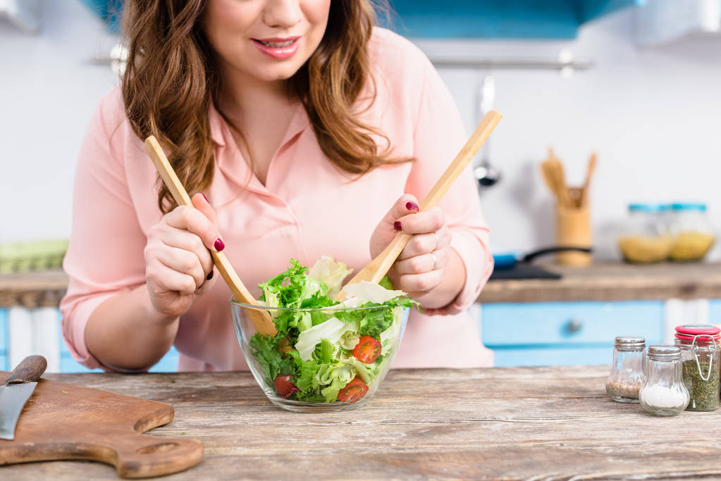 Teilansicht einer übergewichtigen Frau, die zu Hause in der Küche frischen Salat für das Abendessen kocht - Foto, Bild