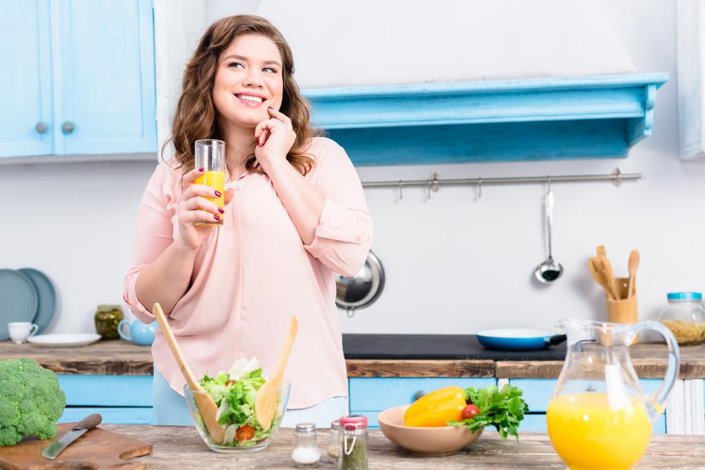 πορτρέτο του υπέρβαρου χαμογελαστό γυναίκα με ποτήρι χυμό στην κουζίνα στο σπίτι - Φωτογραφία, εικόνα