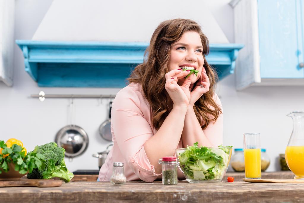 mulher sorrindo sobrepeso à mesa com salada fresca na cozinha em casa
 - Foto, Imagem