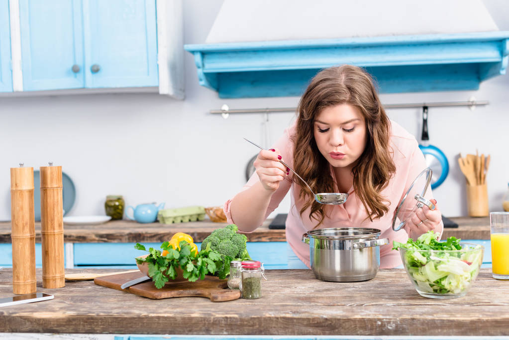 portrét mladé ženy s nadváhou vaření polévky v kuchyni doma - Fotografie, Obrázek