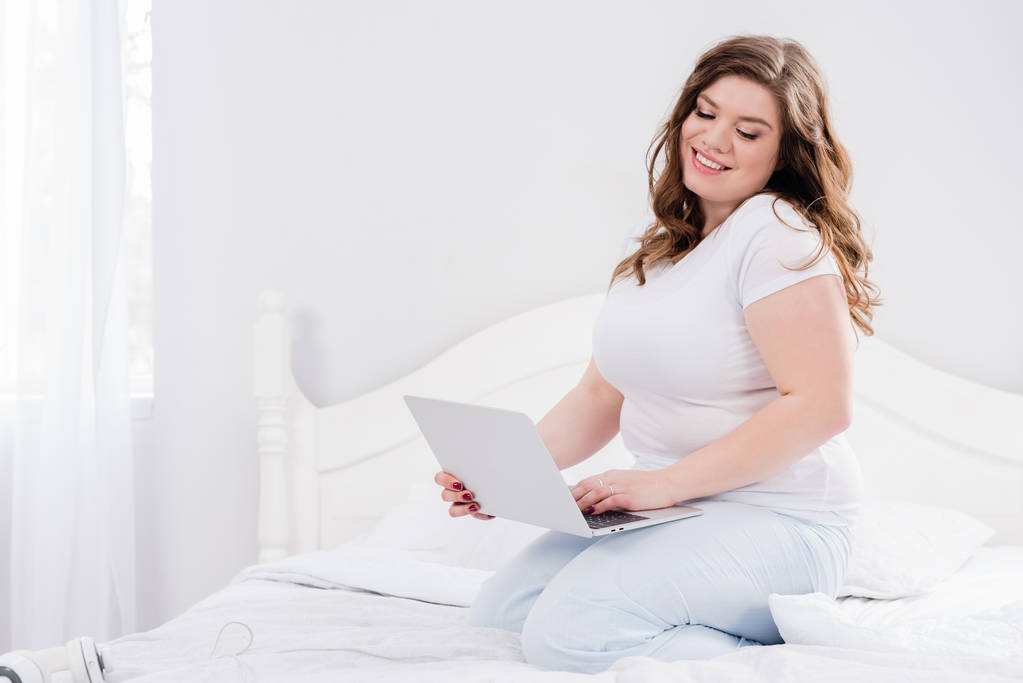donna sorridente in pigiama utilizzando il computer portatile sul letto a casa
 - Foto, immagini