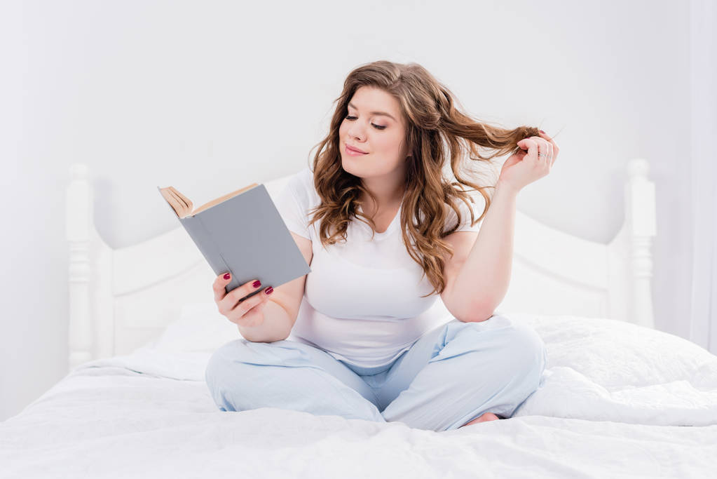 Młoda kobieta w piżamy, czytanie książki na łóżko w domu - Zdjęcie, obraz