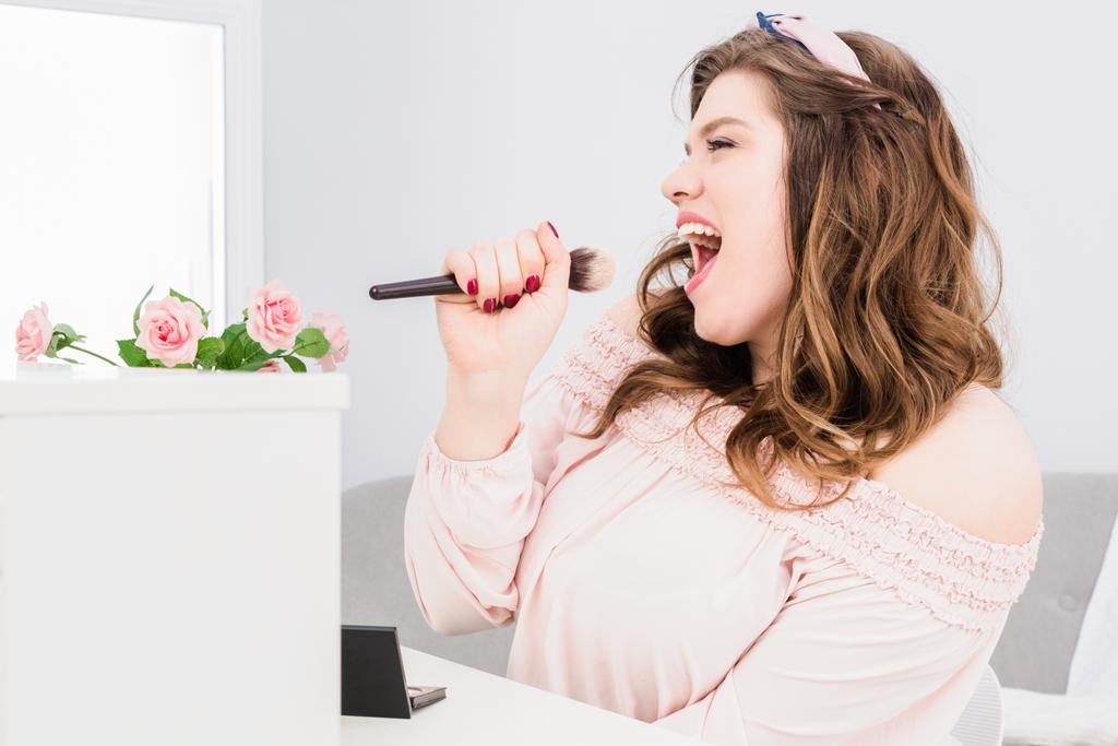 jovem mulher emocional cantando com escova de maquiagem na mão como microfone em casa
 - Foto, Imagem