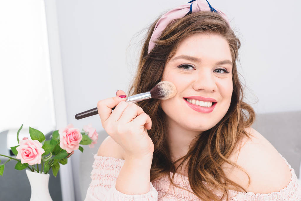 portrait of pretty smiling young woman applying powder while doing makeup at home - Photo, Image