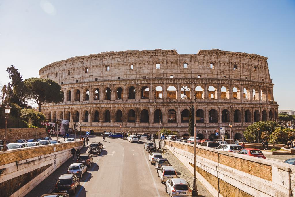 Rome, Olaszország - 2018. március 10.: Colosseum ősi romok napsütéses napon autók parkolnak az utcában - Fotó, kép