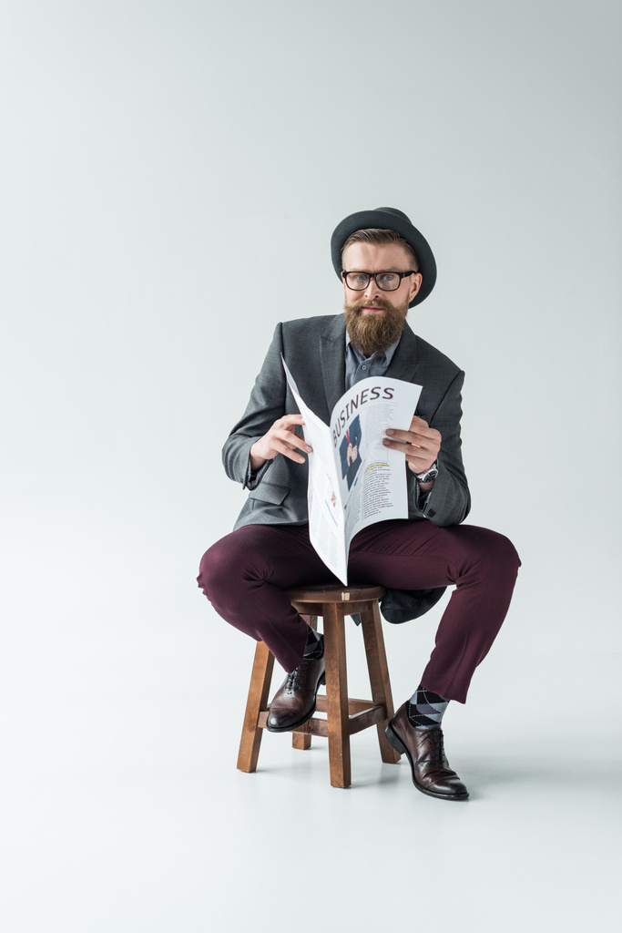 Uomo d'affari con baffi vintage e barba che legge giornali d'affari mentre è seduto su uno sgabello
 - Foto, immagini