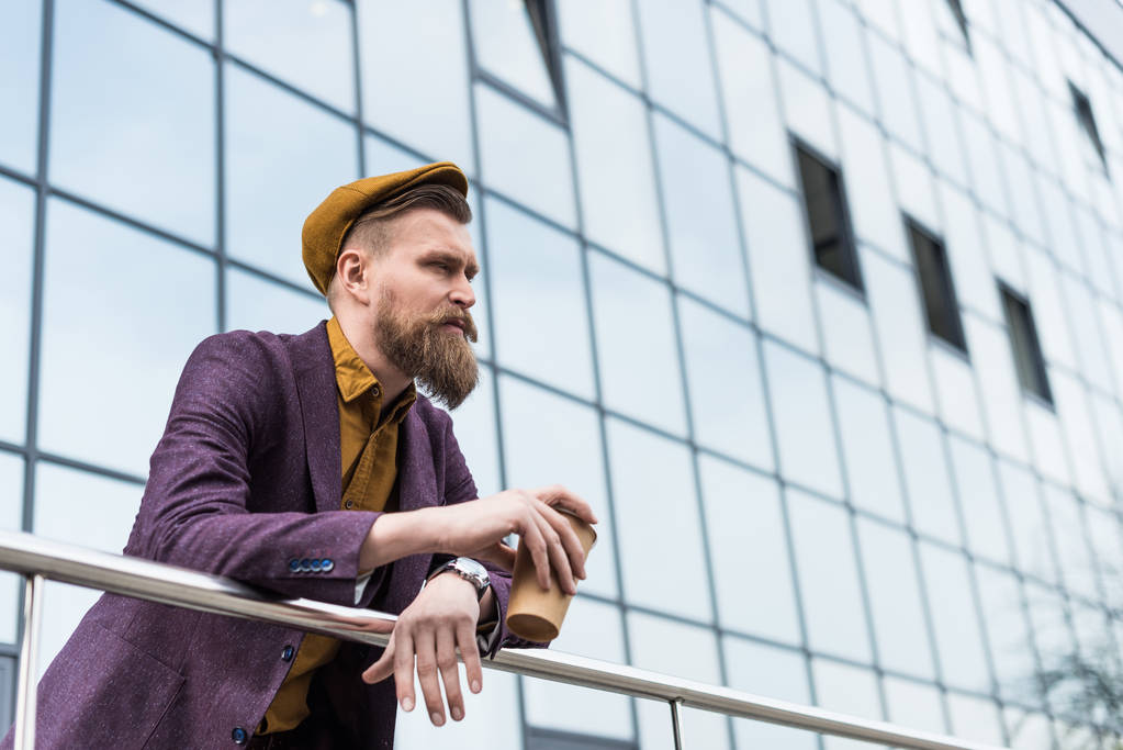 Elegante hombre de negocios barbudo sosteniendo taza de café por edificio moderno
 - Foto, Imagen