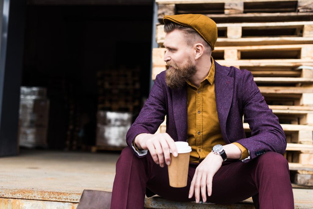 Homem de negócios barbudo elegante sentado na rua com copo de papel nas mãos
 - Foto, Imagem