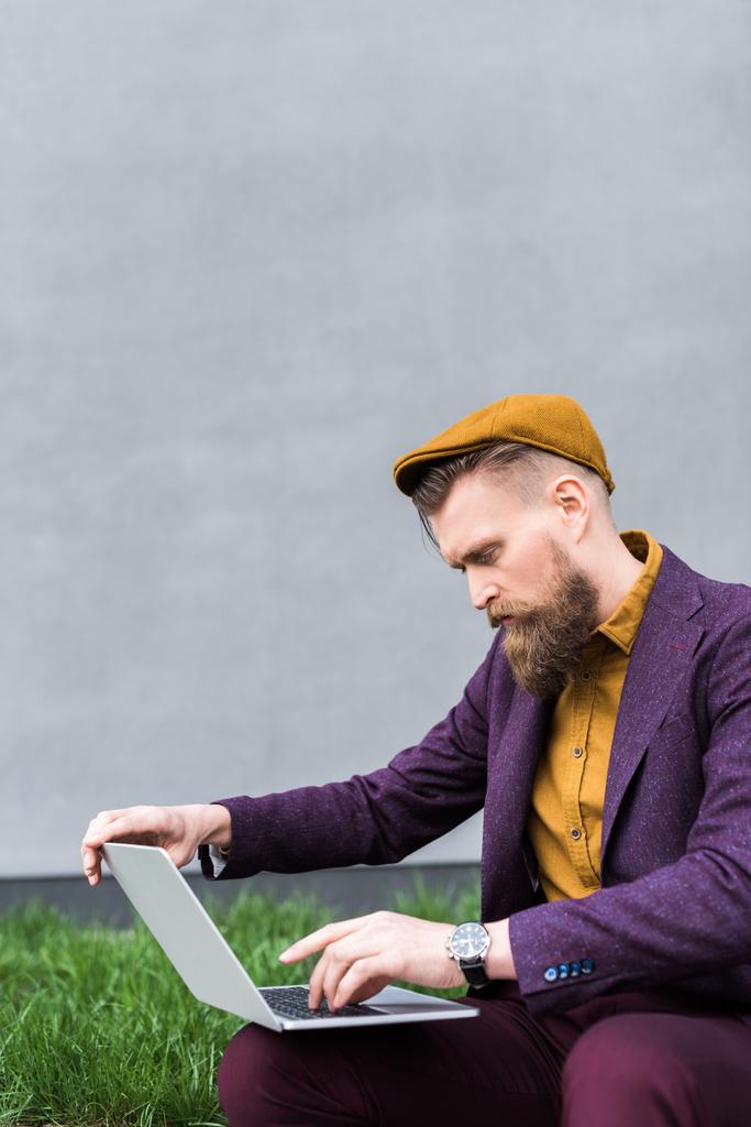 Businessman with vintage mustache and beard sitting on street and looking at laptop - Photo, Image