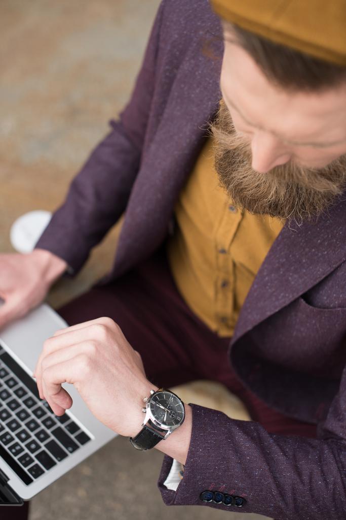 Homme d'affaires avec moustache vintage et barbe travaillant sur ordinateur portable et vérifiant sa montre
 - Photo, image