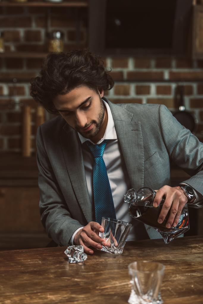 młody człowiek w garnitur wylewanie whisky w szkle - Zdjęcie, obraz