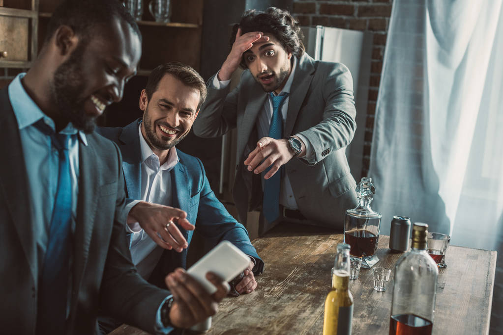 uomo emotivo guardando amici ridenti utilizzando il suo smartphone durante la festa
 - Foto, immagini
