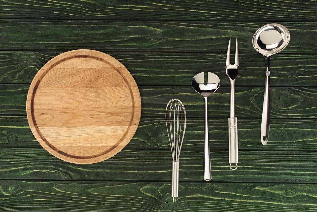vista superior de tabla de cortar de madera redonda y utensilios de cocina metálicos en la mesa
  - Foto, Imagen