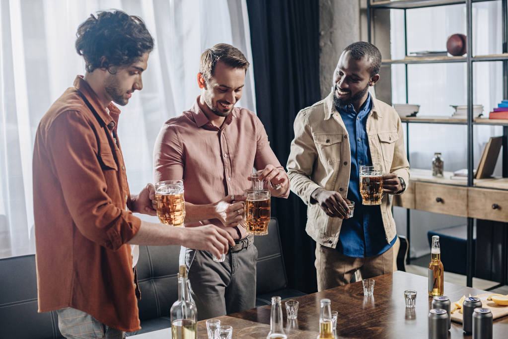 улыбающиеся многонациональные друзья мужчины пьют алкогольные напитки и тусуются вместе
 - Фото, изображение