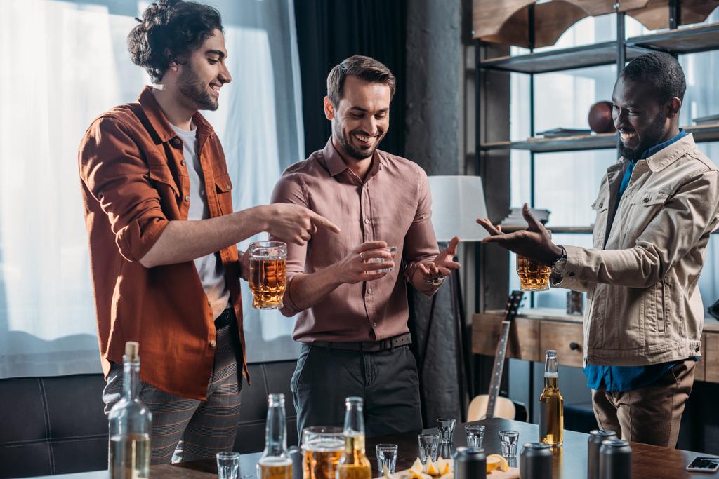 hymyilevät nuoret monikansalliset miehet puhuvat ja juovat alkoholijuomia yhdessä
 - Valokuva, kuva
