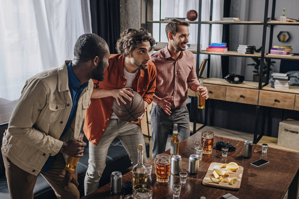 vue latérale d'hommes multiethniques jouant avec le ballon de basket et buvant de la bière ensemble
  - Photo, image