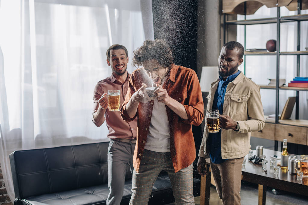 lachende multiethnische Freunde beim Anblick eines Mannes, der Bier aus Dosen trinkt  - Foto, Bild