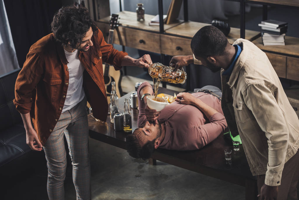 wieloetniczny przyjaciółmi piwo w lejka i człowiek do picia podczas leżenia na stole - Zdjęcie, obraz