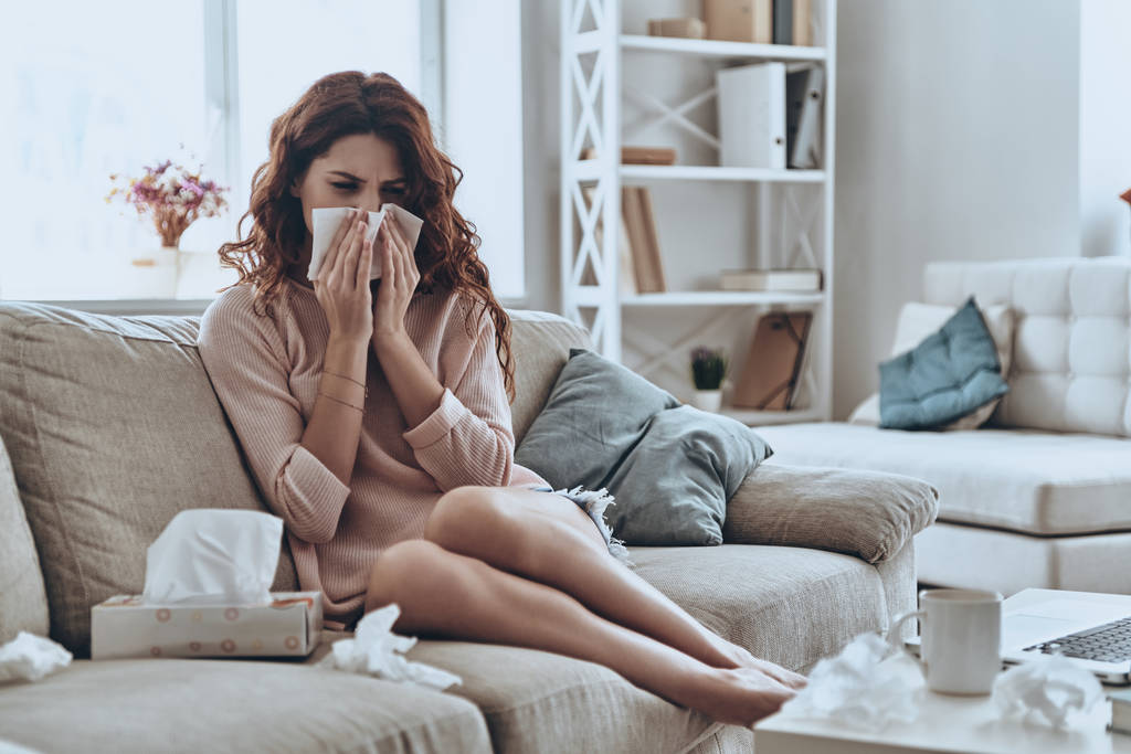 malato giovane donna soffiando il naso utilizzando i tessuti facciali mentre seduto sul divano a casa
    - Foto, immagini