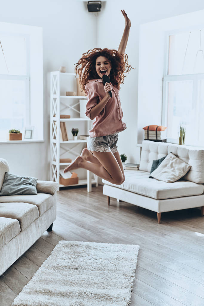 mulher feliz em pijama cantando e pulando no apartamento moderno
 - Foto, Imagem