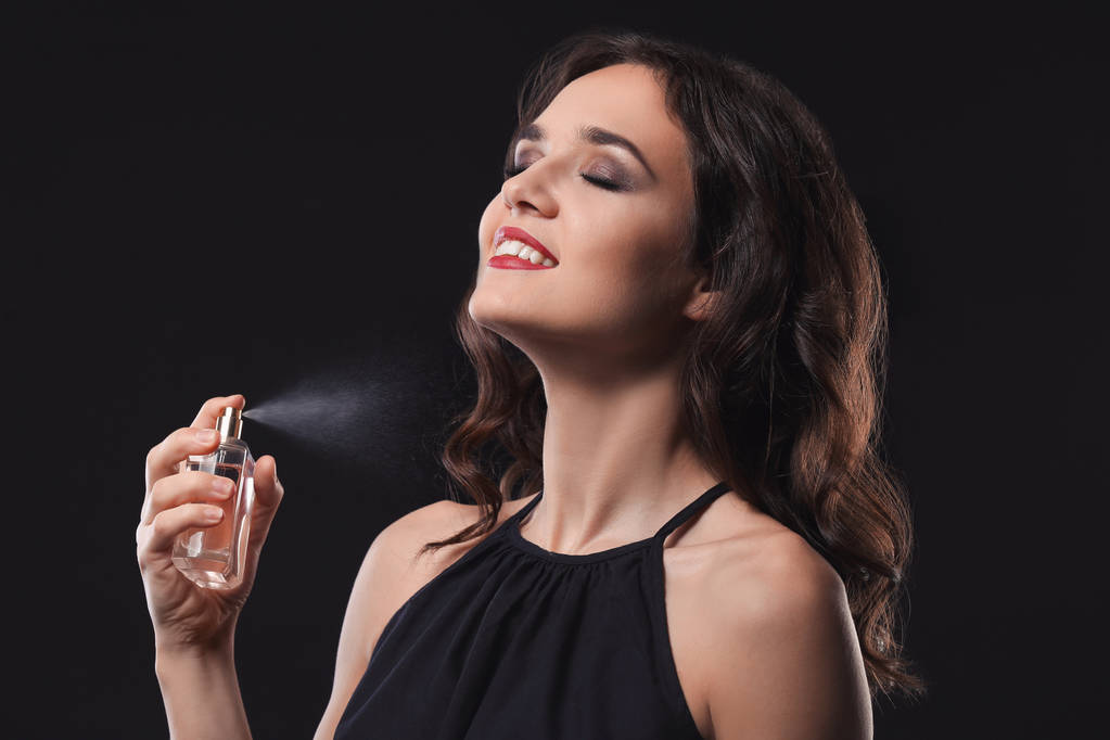 Mooie jonge vrouw met fles parfum op zwarte achtergrond - Foto, afbeelding