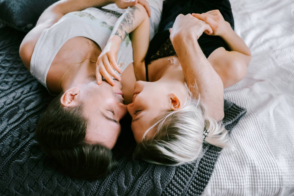 Charmant couple à la maison. Jolie femme et homme séduisant portant des vêtements de maison couché sur un lit, embrasser et étreindre
. - Photo, image