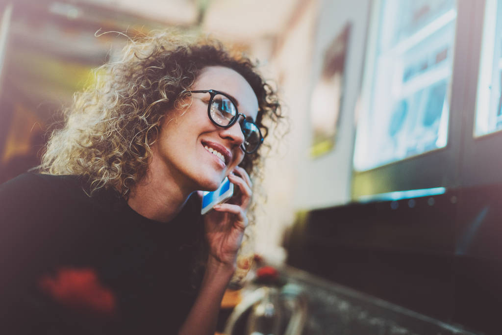 Okouzlující žena, krásný úsměv provedení volání přes její mobilní telefon během odpočinku v kavárně. Efekt bokeh a světlice na rozostřeného pozadí. - Fotografie, Obrázek